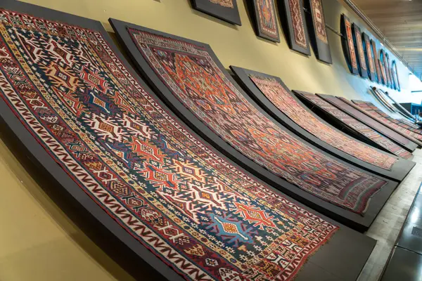 Bir duvarda renkli halılar sergileniyor. Halılar öyle bir düzenlenmiş ki, duvara yaslanmış gibi görünüyorlar. Sahne sıcaklık ve konfordan oluşur.