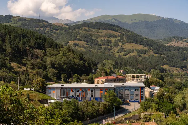Önünde büyük bir bina bulunan bir kasabanın arka planında bir sıradağdır. Bina bir otel ve üzerinde 