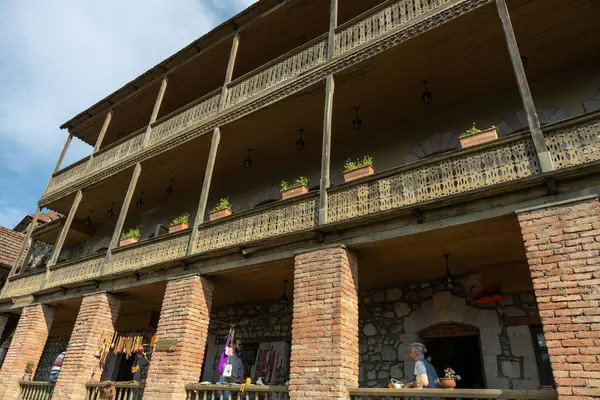 Balkonlu tuğla bir binada bir sürü saksı bitkisi var. Binada dolaşan insanlar var ve bazıları el çantaları taşıyor. Manzara sakin ve huzurlu.