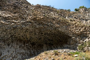 Ortasında mağara olan kayalık bir uçurum. Mağara karanlık ve gökyüzü mavi.