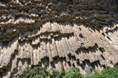Küçük çatlaklar ve çatlaklar olan büyük bir kaya oluşumu. Kaya yosunla kaplı ve pürüzlü bir dokusu var. Güneş ışığı kayaların üzerinde parlıyor, gölgeler yaratıyor.