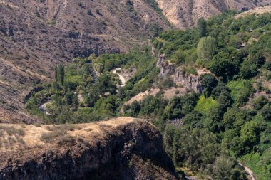 İçinden yol geçen bir dağ ve yanında ağaçlar. Yol dolambaçlı ve ağaçlar yemyeşil