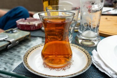 Masadaki bir tabakta bir bardak çay durur. Masa çatal ve bıçak da dahil olmak üzere çeşitli bardaklar ve çatallarla hazırlandı. Sahne sıradan, rahat bir atmosferi işaret ediyor.