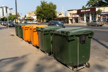Sokakta bir sıra yeşil ve turuncu çöp kutusu sıraya dizildi. Çöp tenekeleri boş ve toplanmayı bekliyorlar. Ortalık sakin ve sakin, etrafta kimse yok.