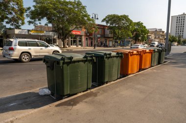 Yolun kenarında bir sıra çöp tenekesi sıraya dizildi. Çöp tenekeleri yeşil, turuncu ve sarı olmak üzere farklı renklerdedir. Sahne arabalarla dolu bir şehirde geçiyor.