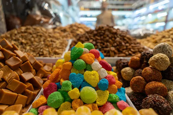 Renkli bir şeker ve çikolata çeşidi bir vitrinde üst üste yığılır. Renklerin ve şekillerin çeşitliliği müşteriler için çekici ve cezbedici bir görüntü yaratır.