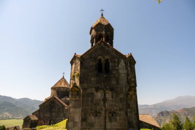 Eski taş binanın bir çan kulesi var ve dağlarla çevrili. Gökyüzü açık ve mavi