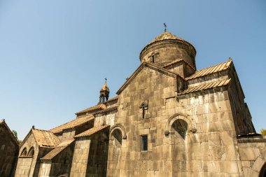 Çan kulesi ve tepesinde haç olan büyük, eski bir bina. Bina bir avluyla çevrili ve üzerinde mavi bir gökyüzü var.