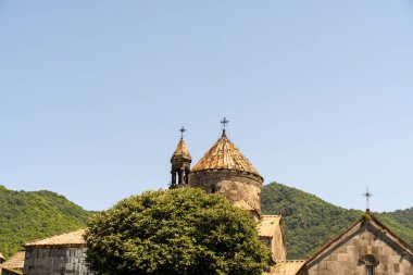 İki kulesi ve çan kulesi olan bir kilise. Gökyüzü açık ve mavi. Kilise ağaçlar ve dağlarla çevrili.