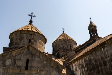 Üç kubbeli binanın tepesinde haçlar var. Gökyüzü açık ve mavi. Binalar eski ve tarih bilinci var.