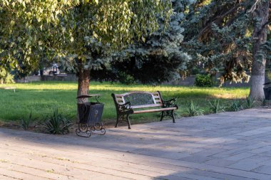 Bir park bankı bir çöp kutusunun önünde oturur. Tezgah boş ve çöp kutusu dolu. Park sessiz ve huzurlu.