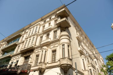 Balkonu ve birkaç penceresi olan büyük beyaz bir bina. Bina yüksek ve bir sürü penceresi var.