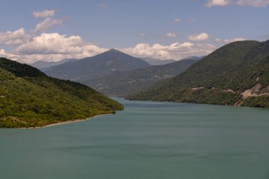 İçinden bir nehir akan güzel bir dağ sırası. Su sakin ve berrak, dağlar yemyeşil ağaçlarla kaplı. Sahne huzurlu ve sakin, dağlarla birlikte.