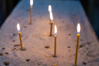 Bir grup mum kumlu bir yüzeye konur. Mumlar art arda dizildi, bazıları diğerlerinden daha uzun. Sahnenin huzurlu ve rahatlatıcı bir atmosferi var.