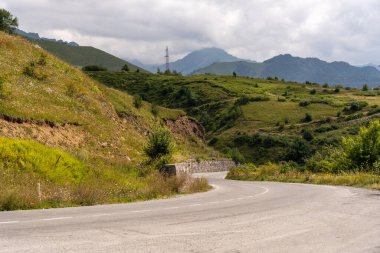 Arka planda dağ olan dolambaçlı bir yol. Yol boş ve gökyüzü bulutlu.