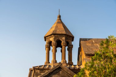 Sivri çatılı ve tepesinde haç olan yüksek bir bina. Bina ağaçlarla çevrili ve arka planda mavi bir gökyüzü var.