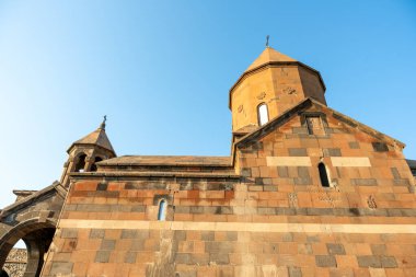Arka planda mavi gökyüzü ve çan kulesi olan büyük bir bina. Bina taştan yapılmış ve bir sürü penceresi var.