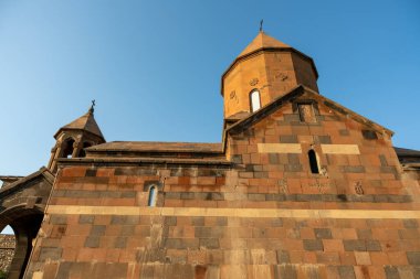 Çan kulesi ve tepesinde haç olan büyük bir bina. Bina taştan yapılmıştır ve birçok penceresi vardır. Gökyüzü mavi ve berrak