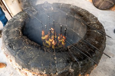 Büyük, siyah, içinde ateş olan yuvarlak bir çukur. Çukur et ve sebzelerle dolu.