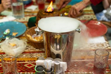 Duman dolu gümüş bir kova bir grup insanla bir masada oturur. Ortam rahat ve rahat. Masanın etrafında oturan insanlar birbirlerinin arkadaşlığından keyif alıyorlar.