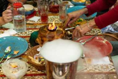 Üzerinde pasta olan bir masa ve onu kesen biri. Pasta tabaklar ve fincanlarla çevrili.