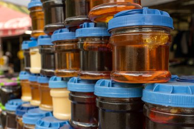 Farklı renklerde kapaklı kavanoz yığını. Kavanozlar çeşitli bal çeşitleriyle dolu.