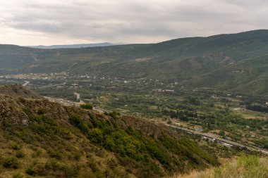 Aşağıdaki vadide bir kasabası olan bir dağ sırası. Gökyüzü bulutlu ve dağlar ağaçlarla kaplı.