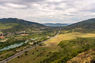 Yanı başında nehir akan bir yol. Yol boş ve gökyüzü bulutlu.