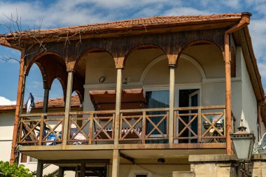 Balkonlu bir evin ahşap korkulukları vardır. Korkuluk kemerlerle süslenmiş ve kahverengi bir gölgeliği var. Ev güneşli bir bölgede bulunuyor.