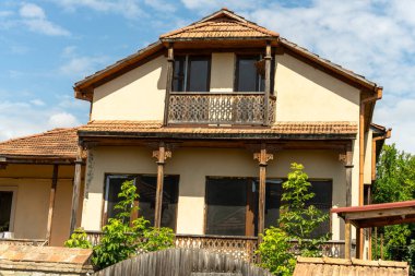 Kırmızı çatılı ve balkonlu büyük bir ev. Ev ağaçlarla çevrili ve bir sürü penceresi var.