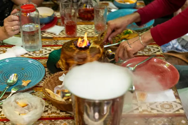 Üzerinde pasta olan bir masa ve onu kesen biri. Pasta tabaklar ve fincanlarla çevrili.