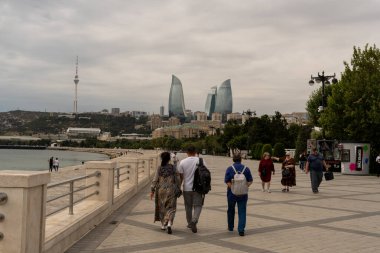 Bir grup insan büyük bir binanın yanındaki kaldırımdan aşağı yürüyor. Gökyüzü bulutlu ve güneş görünmüyor.
