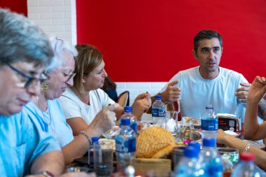 Bir grup insan bir masada oturup yiyor ve içiyor. Masada birkaç şişe su ve birkaç fincan var. Sahne rahat ve rahat.