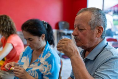 Bir adam ve bir kadın masada oturmuş bardaktan içiyorlar. Adam mavi bir gömlek giyiyor ve kadın mavi bir gömlek giyiyor. Sahne rahat ve sıradan.
