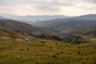 Arkasında dağ sıraları olan engin, açık bir alan. Gökyüzü bulutlu ve atmosfer sakin.
