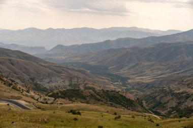 Dağlar ağaçlarla kaplı ve gökyüzü bulutlu. Manzara huzurlu ve huzurlu.