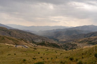 İçinden geçen bir yolu olan bir dağ sırası. Gökyüzü bulutlu ve dağlar ağaçlarla kaplı.