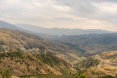 Dağlar ağaçlarla kaplı ve gökyüzü bulutlu. Manzara çok güzel ve huzurlu.