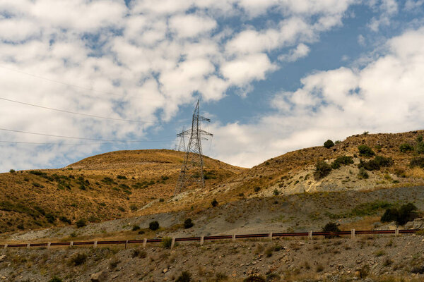 Башня линии электропередач на склоне холма. Небо облачно, и солнце светит.