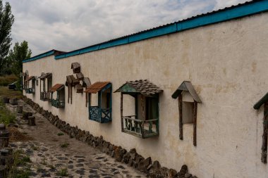 Mavi çatıları olan bir sıra küçük ev taş bir duvarda duruyor. Evler ahşaptan yapılmış ve küçük pencereleri var. Sahne huzurlu ve antika.
