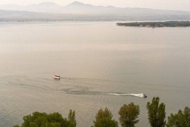 İçinde birkaç kişi olan bir tekne sudadır. Su sakin ve gökyüzü bulutlu.