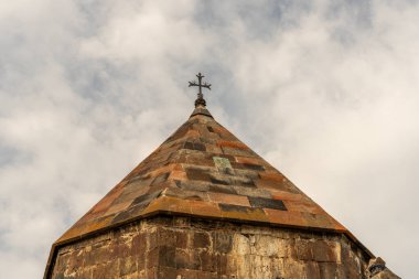 Tepesinde haç olan taş bir bina. Bina eski ve kırsal bir görünüme sahip. Gökyüzü bulutlu ve güneş görünmüyor.