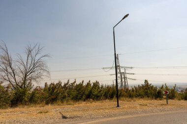 Üstünde sokak lambası olan bir direk. Direk siyah ve ışık beyaz. Gökyüzü mavi ve hiç bulut yok.