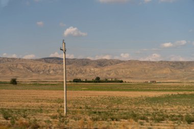 Arka planda bulutlu bir gökyüzü olan bir tarlada bir direk duruyor. Gökyüzü mavi ve sırık uzun