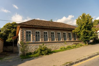 Bir sürü penceresi ve eğimli çatısı olan büyük bir tuğla ev. Ev ağaçlarla çevrili ve ona doğru uzanan taş bir geçidi var.