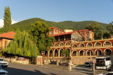 Kemerli pencereli ve kırmızı çatılı bir bina. Bina ağaçlarla çevrili ve büyük bir avlusu var.