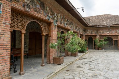 Tuğla bina ve bank olan bir avlu. Avlu boş ve huzurlu bir atmosferi var.