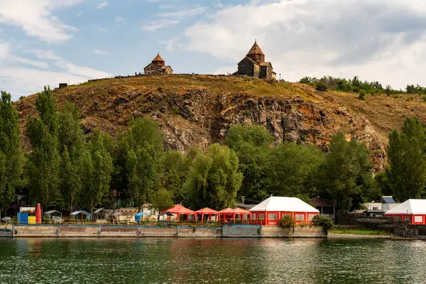 Arkasında büyük bir tepe olan güzel bir kasaba manzarası. Tepe ağaçlarla kaplı ve tepesinde bir şato var. Kasabanın içinden akan bir nehir var ve birkaç bina var.