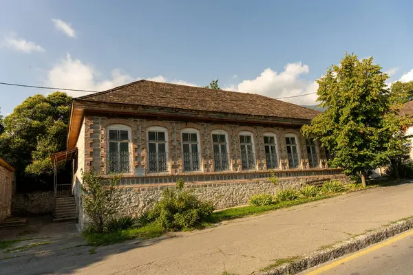 Bir sürü penceresi ve eğimli çatısı olan büyük bir tuğla ev. Ev ağaçlarla çevrili ve ona doğru uzanan taş bir geçidi var.