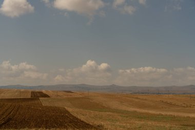 Arka planda bulutlu bir gökyüzü olan bir toprak tarlası. Gökyüzü çoğunlukla mavi ve birkaç bulut etrafa saçılmış.
